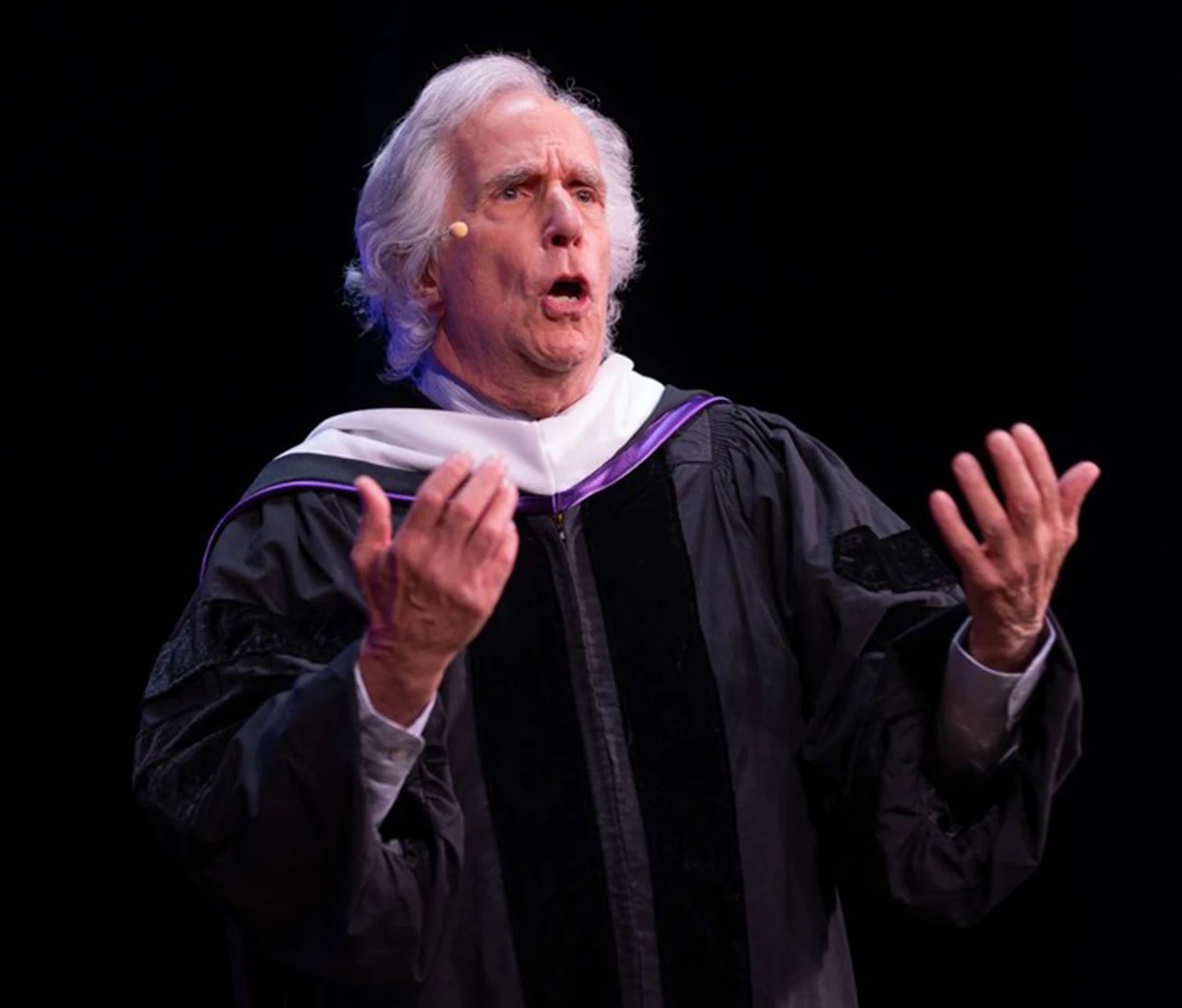 Henry Winkler gestures while delivering the keynote address in academic regalia at Emerson College Commencement.