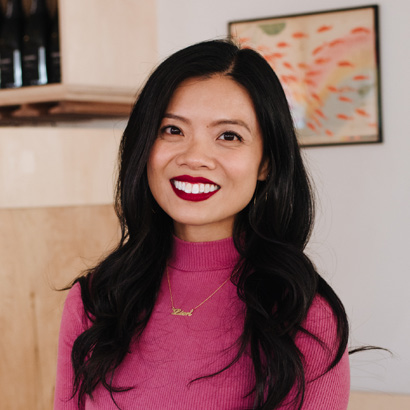 Portrait of Lien Ta wearing a bright pink top and smiling indoors.
