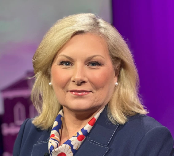 Headshot of Marilyn Schairer wearing a navy blazer and patterned scarf against a purple studio background.