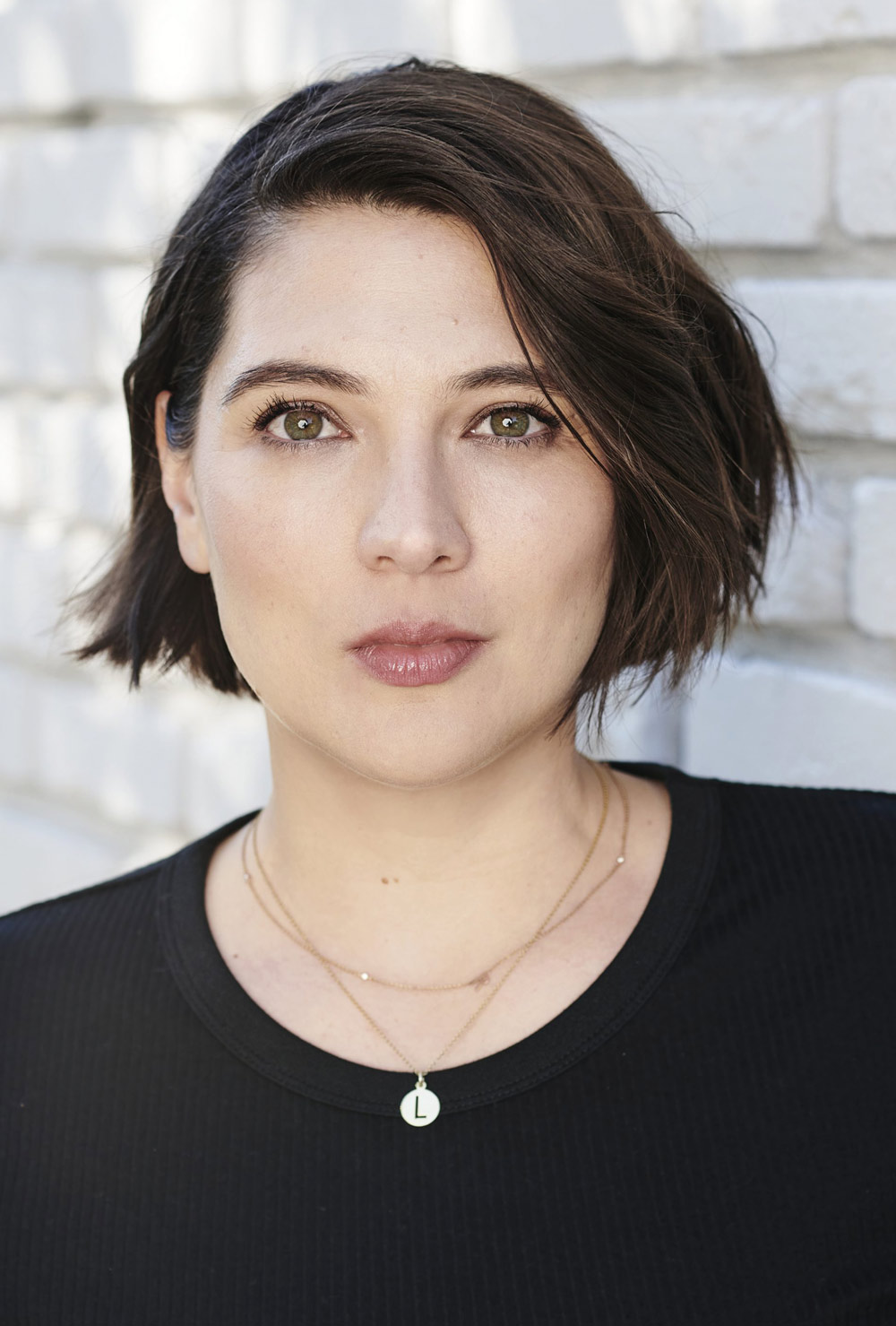 Close-up portrait of Taylor Jenkins Reid with short dark hair, wearing a black top and a delicate gold pendant necklace.