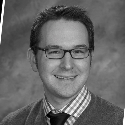 Black-and-white studio headshot of Eric Cornell wearing glasses, a tie, and sweater.