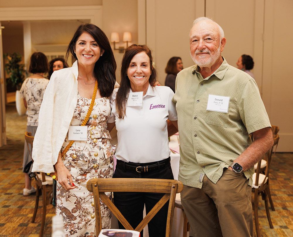 Two women and a man with name tags smile while posing together at an event.
