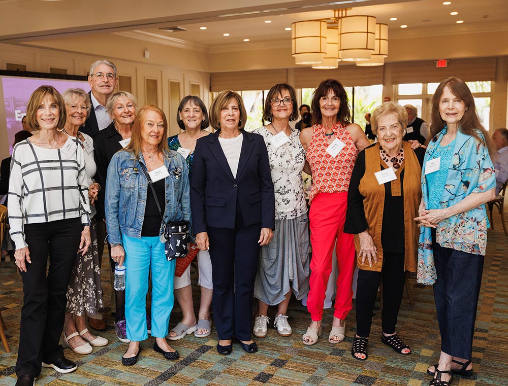 Alumni in Florida wearing name tags smile and pose together in a room at Emerson in Boca Raton.