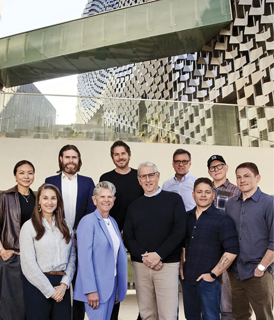 Ten people pose together outside Emerson College Los Angeles, with the campus’s geometric facade behind them.